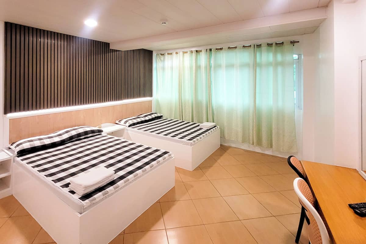 Ein Hotelzimmer mit zwei Betten, einem hölzernen Kopfstück, einem kleinen Tisch und einem Fenster mit Vorhängen.