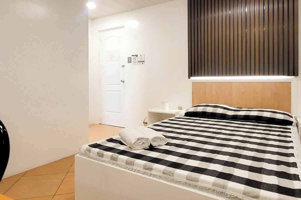 Ein Hotelzimmer mit Bett, Nachttisch, weißer Tür und Holz-Kopfteil.