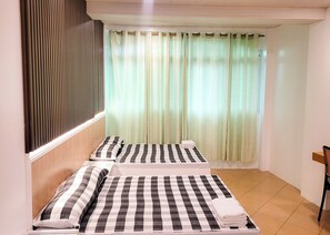 Une chambre d’hôtel avec deux lits, chacun doté de draps à rayures, une fenêtre avec des rideaux légers et une tête de lit en bois.