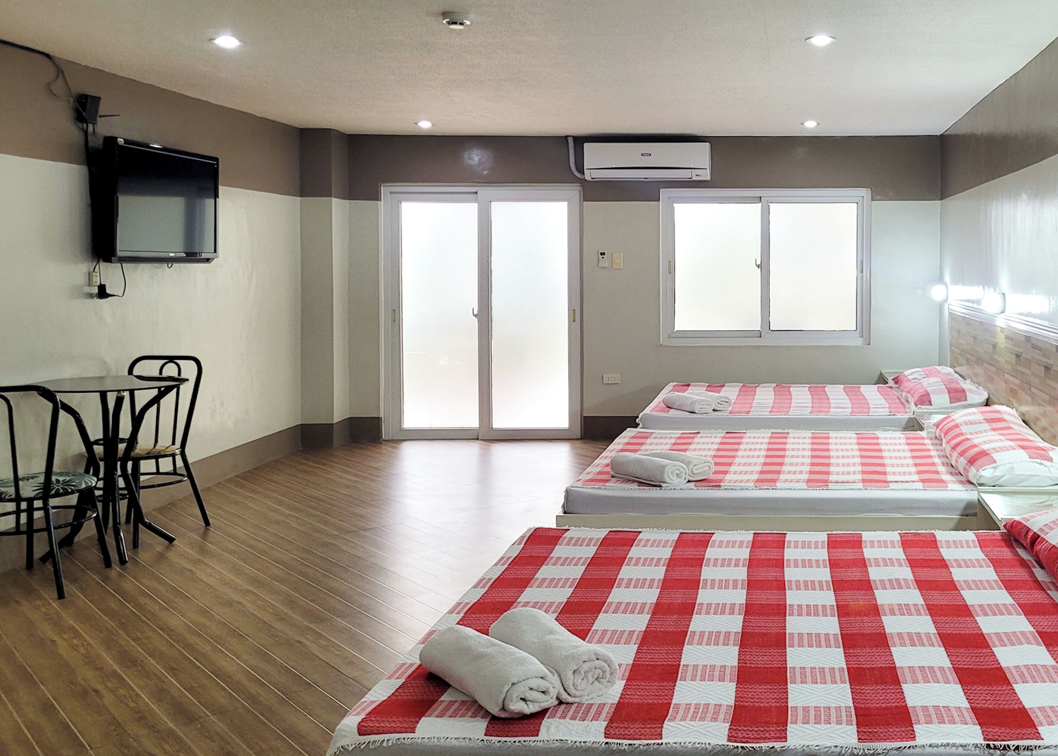 Una habitación de hotel con dos camas, un televisor, una mesa con sillas y una puerta corrediza.
