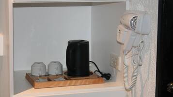 A hotel room with a coffee maker, a hair dryer, and a telephone on a shelf.