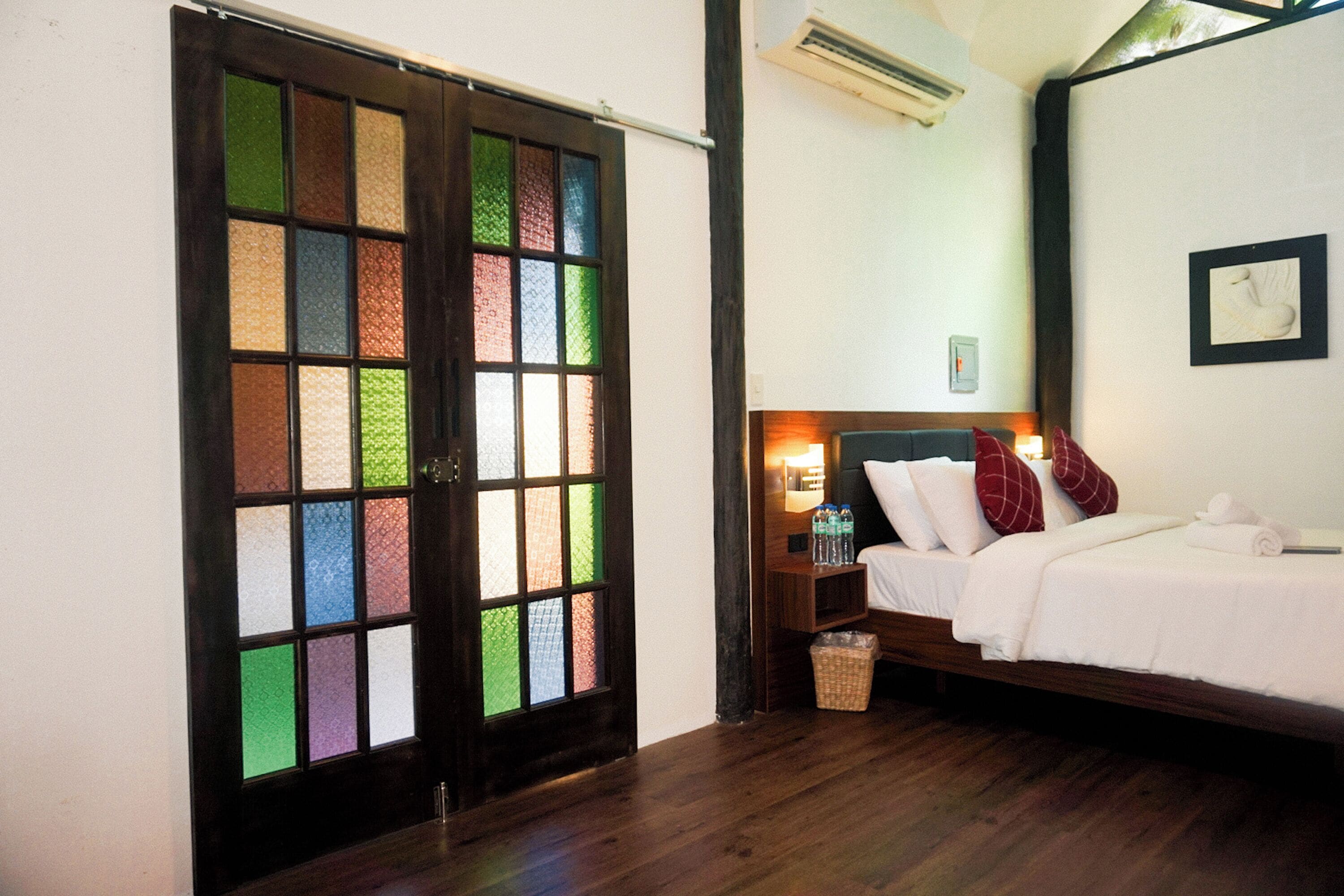 A room with a bed, a nightstand, a wall-mounted air conditioner, and a door with colorful glass panels.