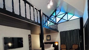 A hotel room with a large bed, a TV, a desk, and a balcony with a view. - Ilocos Urban Wave Resort Hotel (Laoag)