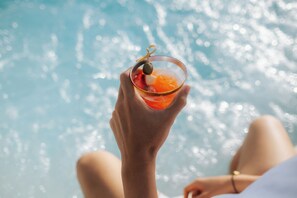 Una persona sosteniendo un cóctel con aceituna, con una piscina al fondo.
