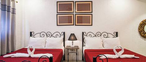 A hotel room with two beds, each with a red bedspread and white pillows, a small table with a lamp, and a ceiling fan.