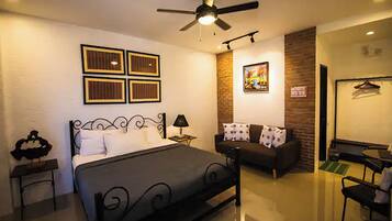 Une chambre à coucher comprenant un lit, une table de chevet, un bureau, un canapé, un ventilateur de plafond et un mur décoré de tableaux encadrés.