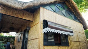 A building with a thatched roof, bamboo walls, and a large window with a decorative awning. - Ilocos Urban Wave Resort Hotel (Laoag)