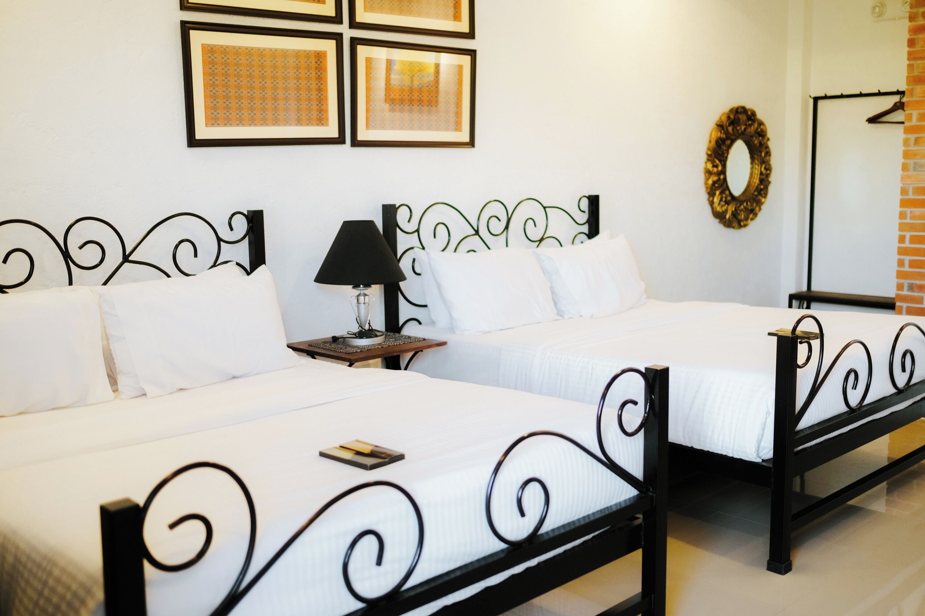A hotel room with two beds, a nightstand, a lamp, framed pictures on the wall, and a mirror.