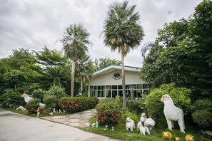A building with a green roof and large windows, surrounded by lush greenery and various animal sculptures. - Rung Rueng Resort (Chonnabot)
