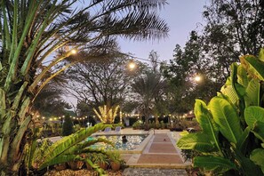 A pool area with a pathway, surrounded by lush greenery and string lights. - Rung Rueng Resort (Chonnabot)