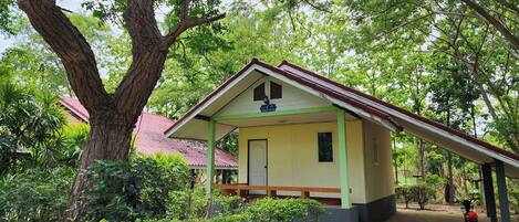 A small, single-story building with a sloped roof, surrounded by lush greenery and trees.