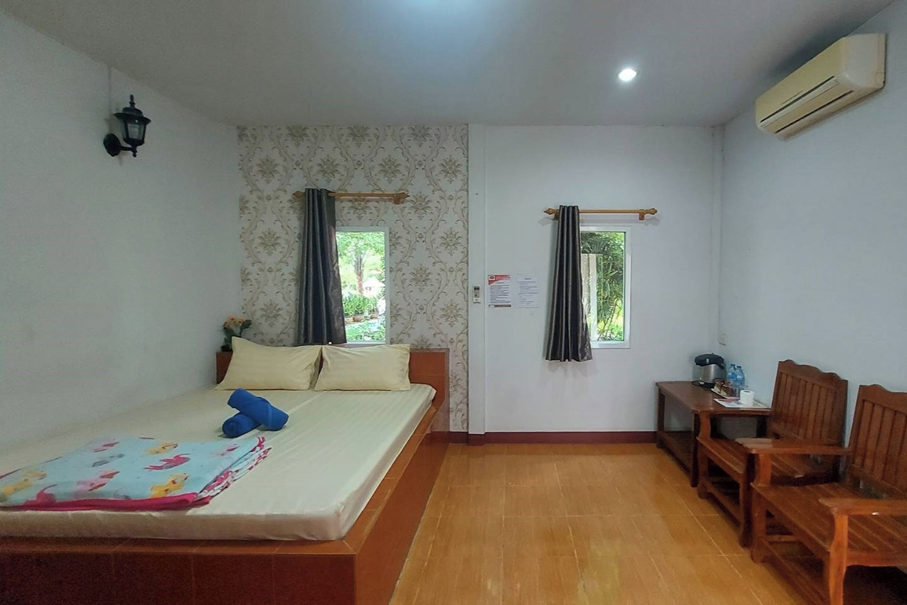 Um quarto com uma cama, um banco de madeira, uma mesinha e um aparelho de ar condicionado.