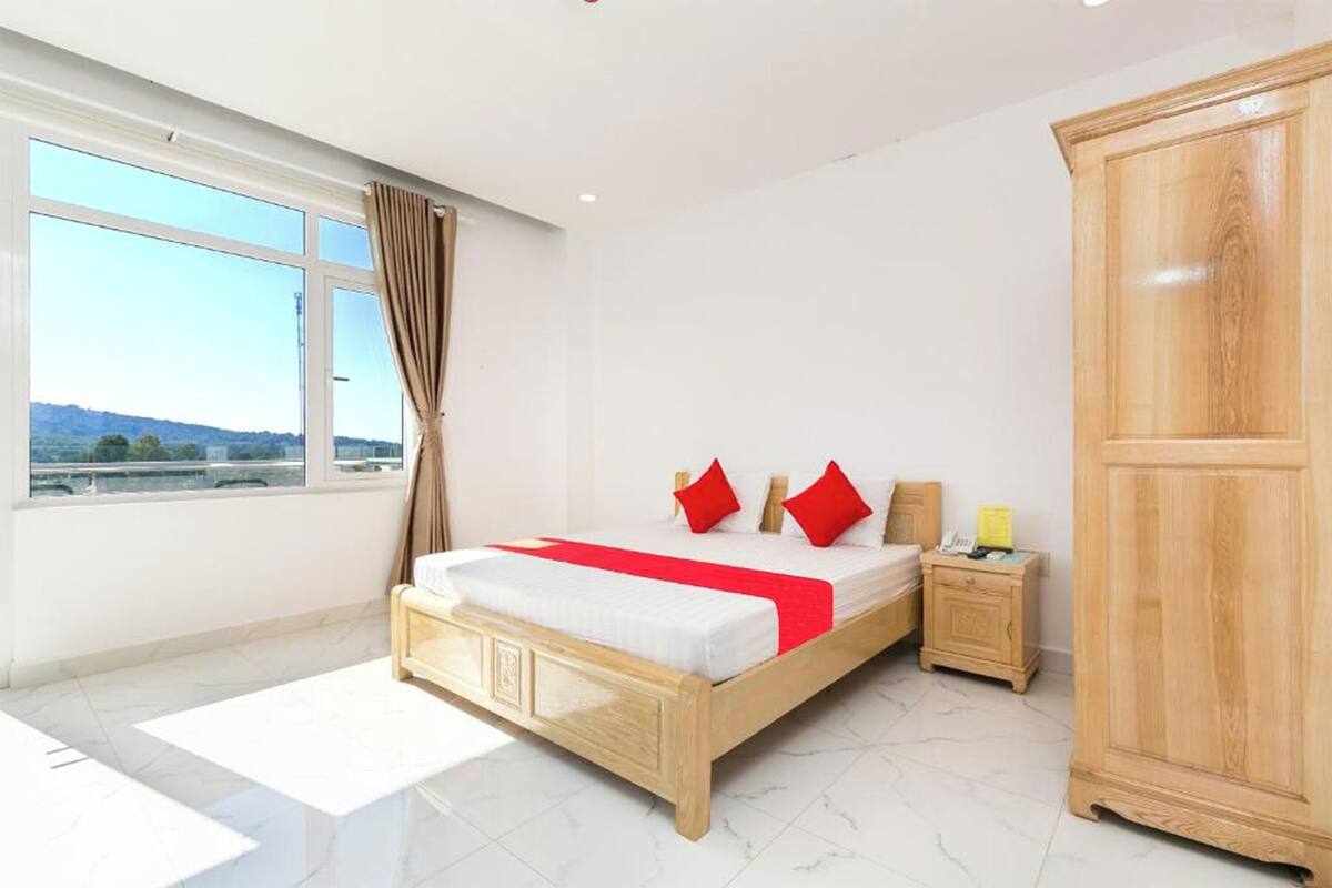 A modern bedroom with a large bed, a wooden wardrobe, a nightstand, and a view of the outside.