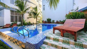 Une piscine avec des marches carrelées, des chaises longues et des palmiers.