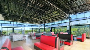 Un vaste espace intérieur doté de sièges rouges et noirs, de grandes fenêtres et d’une structure de toit en métal.