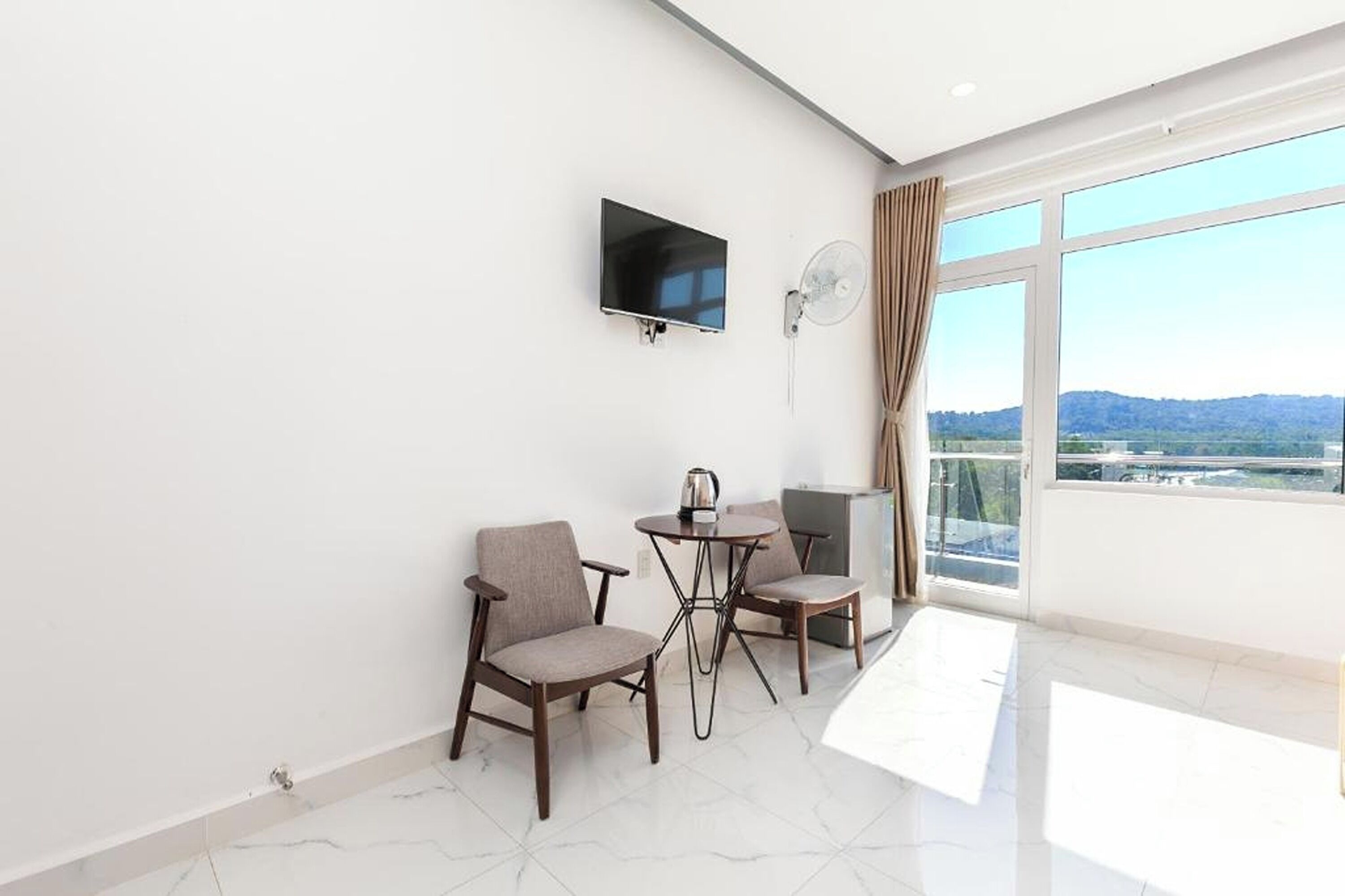 A modern room with a flat-screen TV, two chairs, a small table, and a large window with a view of the landscape.