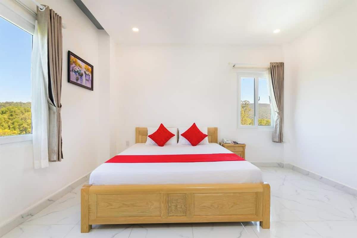 A bedroom with a large bed, a nightstand, a window with curtains, and a painting on the wall.