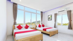 Une chambre d’hôtel avec deux lits en bois, du linge de lit blanc, des oreillers rouges et des rideaux beiges.