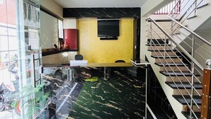 A reception area with a marble counter, a reception desk, a yellow textured wall, and a staircase with metal railings. - Marvel Comforts Near Fortis Hospital, Bannerghatta Road (Bengaluru)