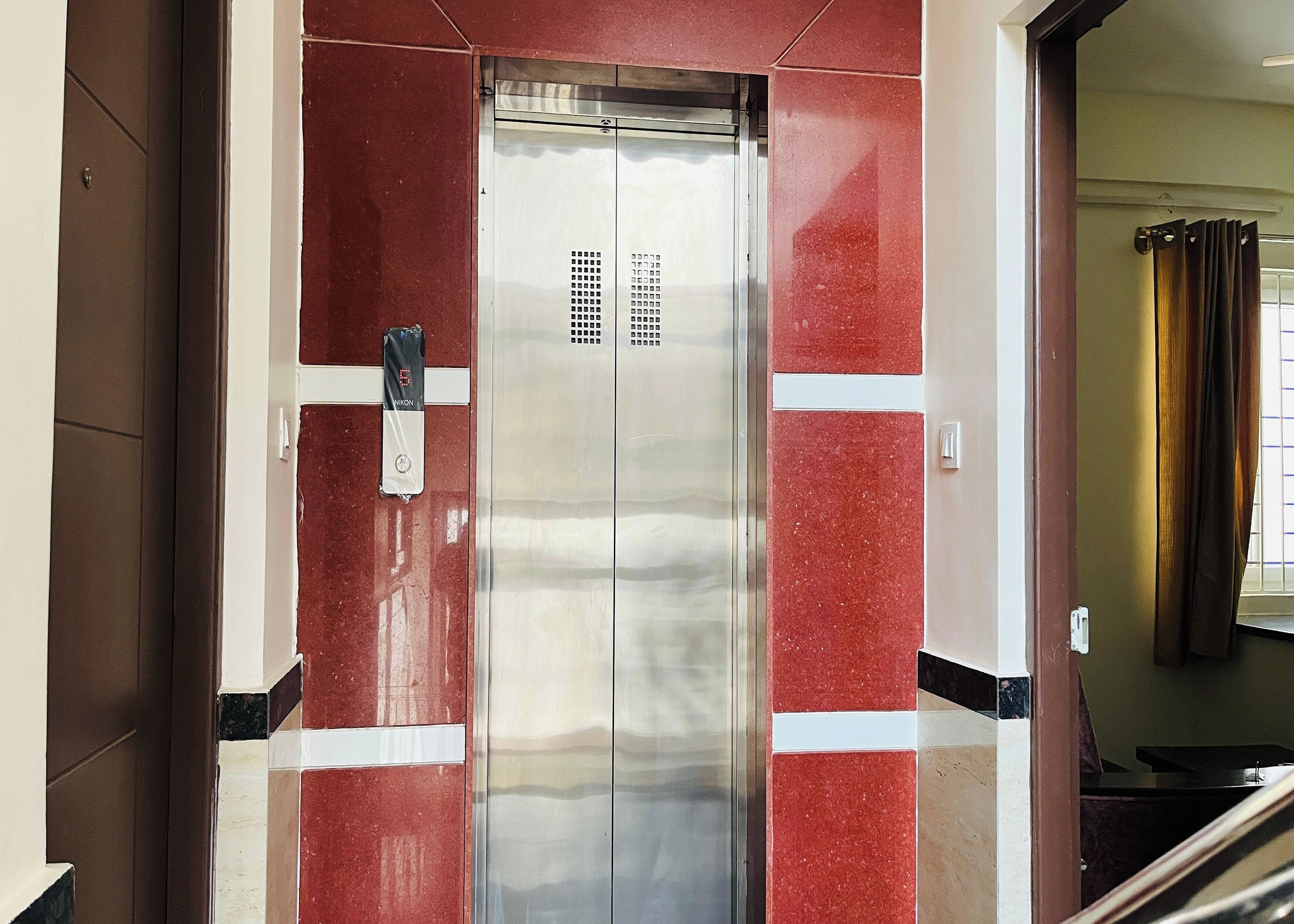 An elevator with a metallic finish and red-tiled walls.