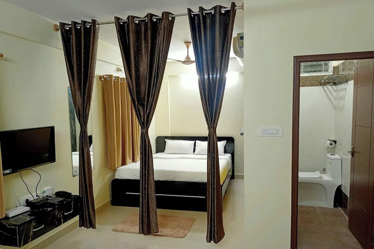 Una habitación de hotel con cama, cortinas, televisión y baño visible a través de una puerta abierta.