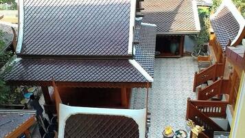 A traditional Thai house with a tiled roof, wooden staircase, and a small garden area.