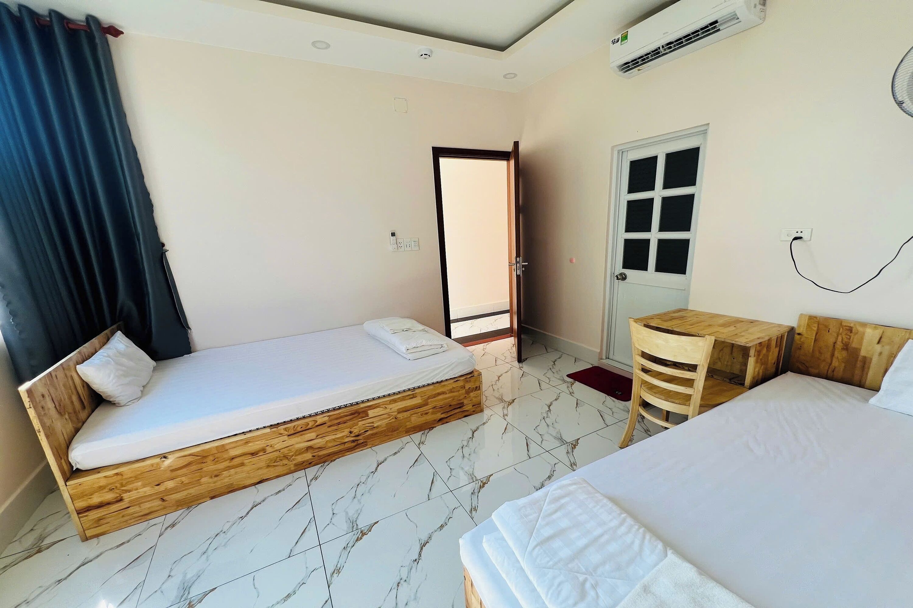 A room with a wooden bed, a smaller bed, a wooden desk, a chair, and a door.
