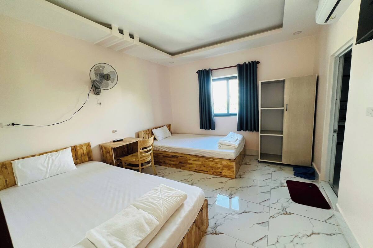 A room with two beds, a desk, a chair, a wardrobe, and a window with curtains.