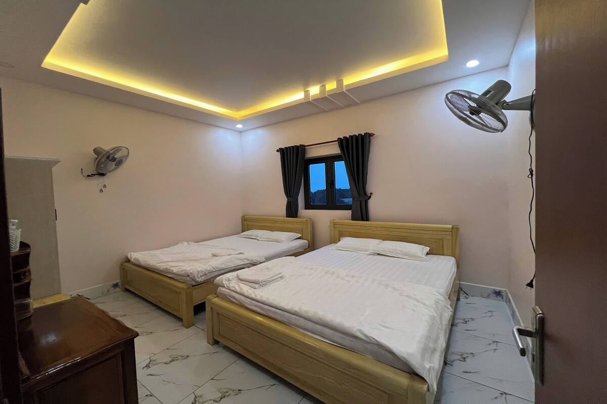A hotel room with two wooden beds, a ceiling fan, and a window with curtains.