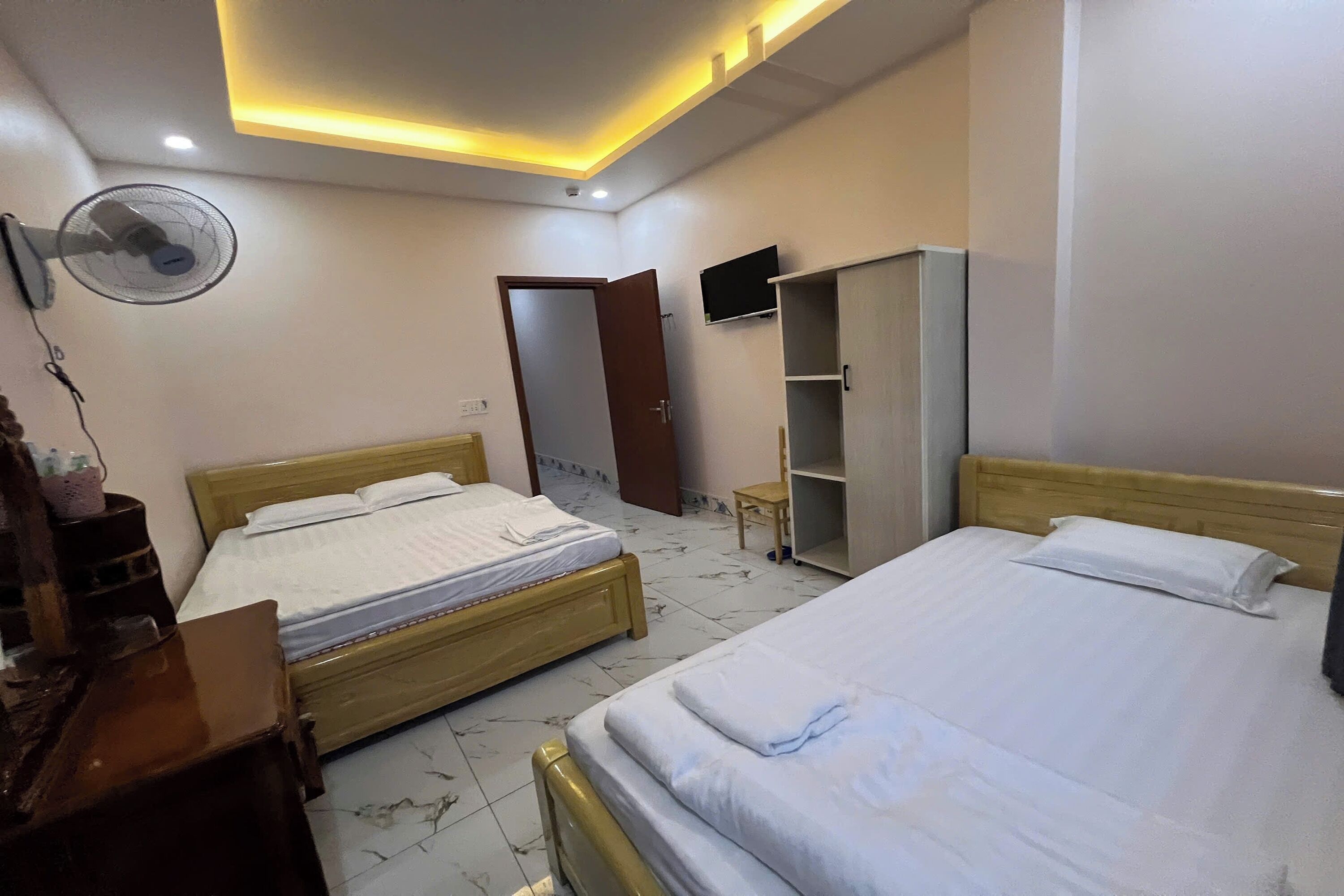 A bedroom with two beds, a wardrobe, a TV, and a ceiling fan.