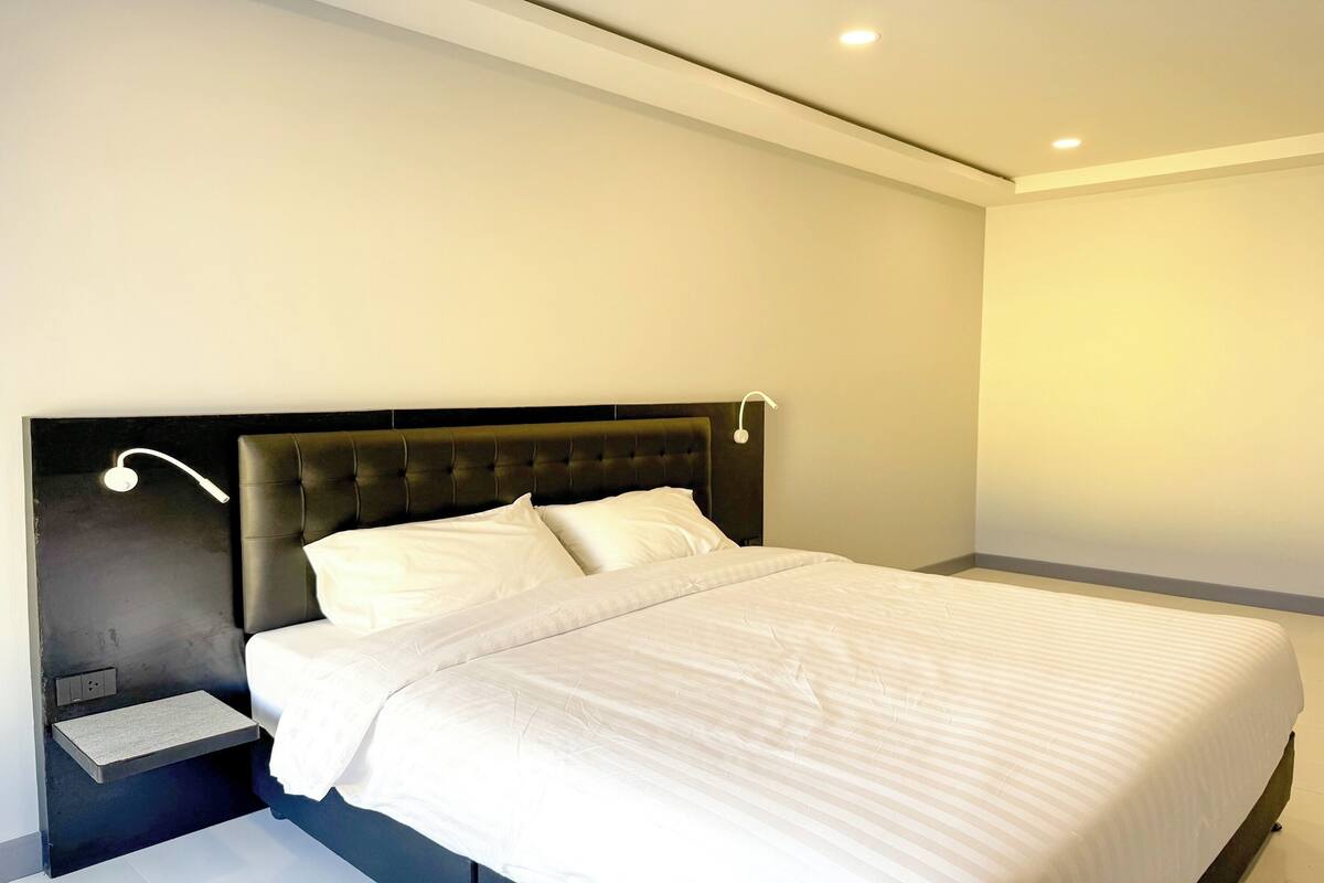 A modern bedroom with a large bed, a nightstand, and a wall-mounted reading light.