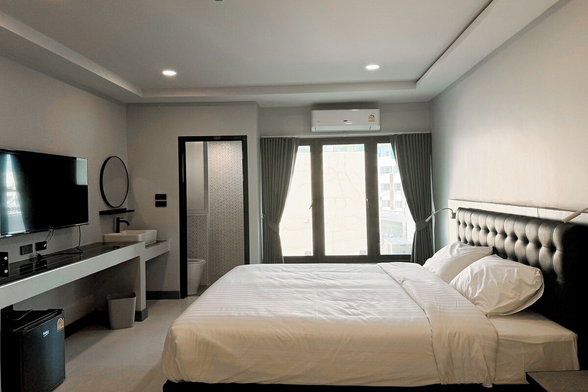A modern hotel room with a bed, a TV, a desk, and a bathroom.
