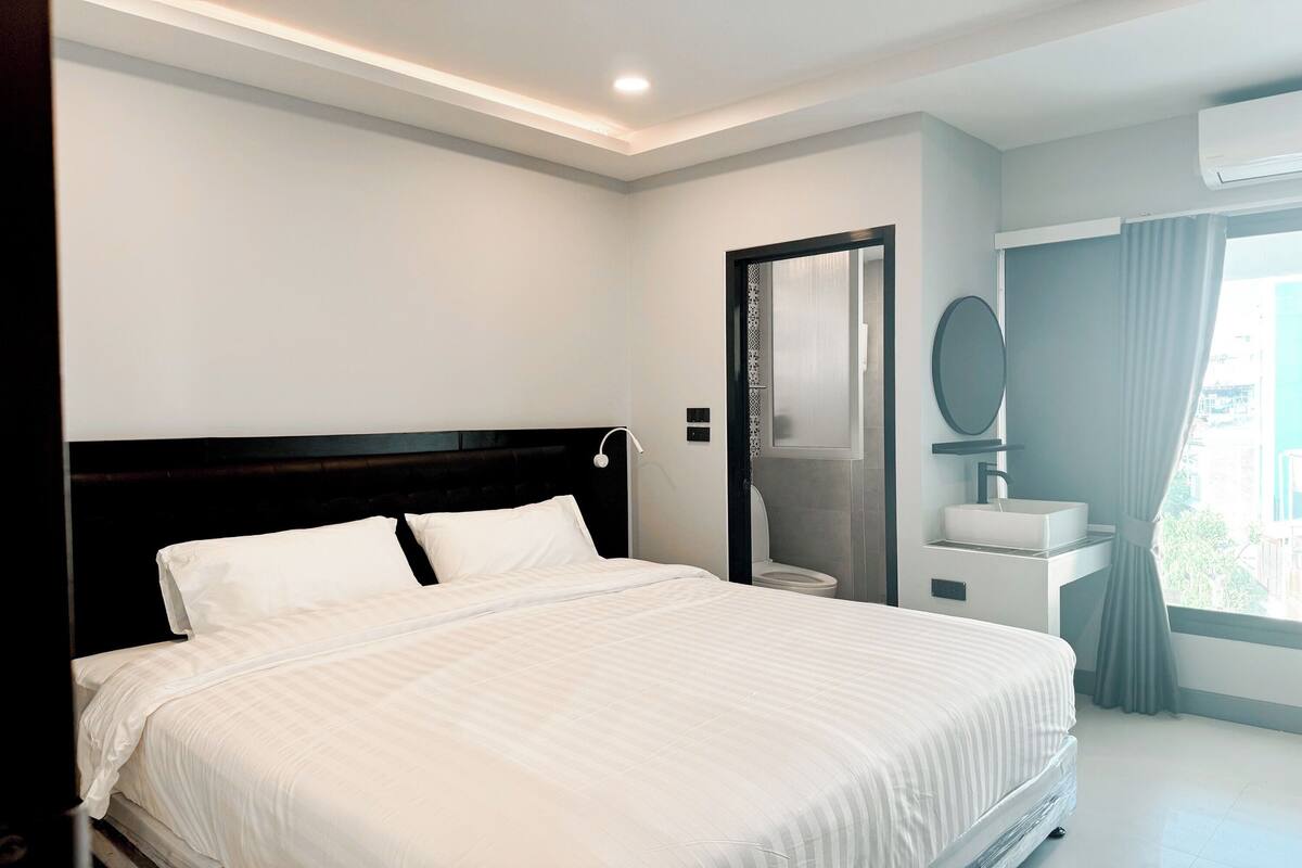A modern hotel room with a large bed, a bedside table, a mirror, and a window with curtains.