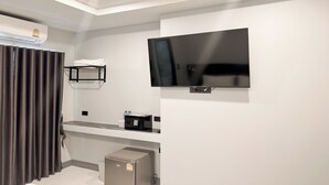 A modern bathroom with a flat-screen TV mounted on the wall, a towel rack, a small shelf, and a compact refrigerator. - Smith Hotel (Chiang Mai)