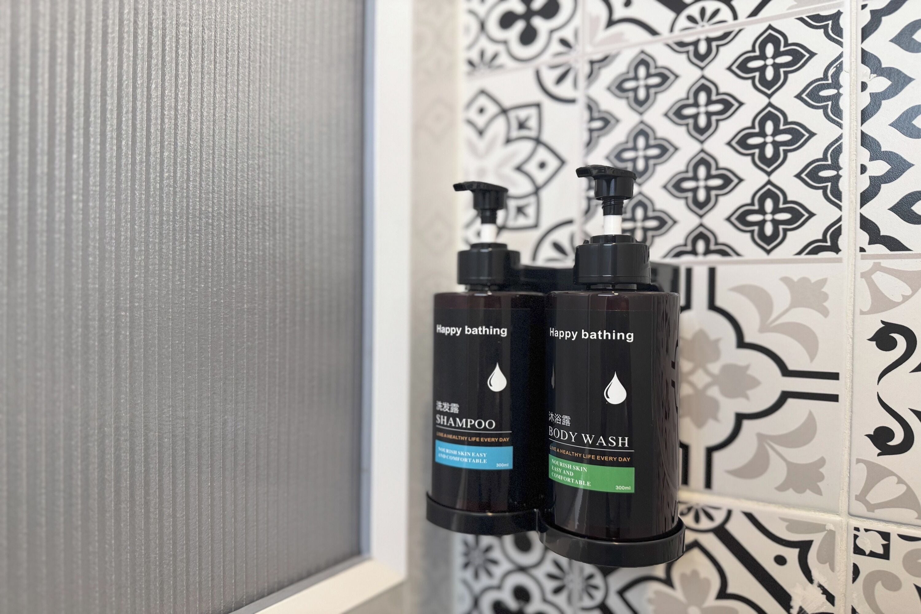 Deux bouteilles de shampoing et de gel douche « Happy Bathing » sont posées sur un mur carrelé.
