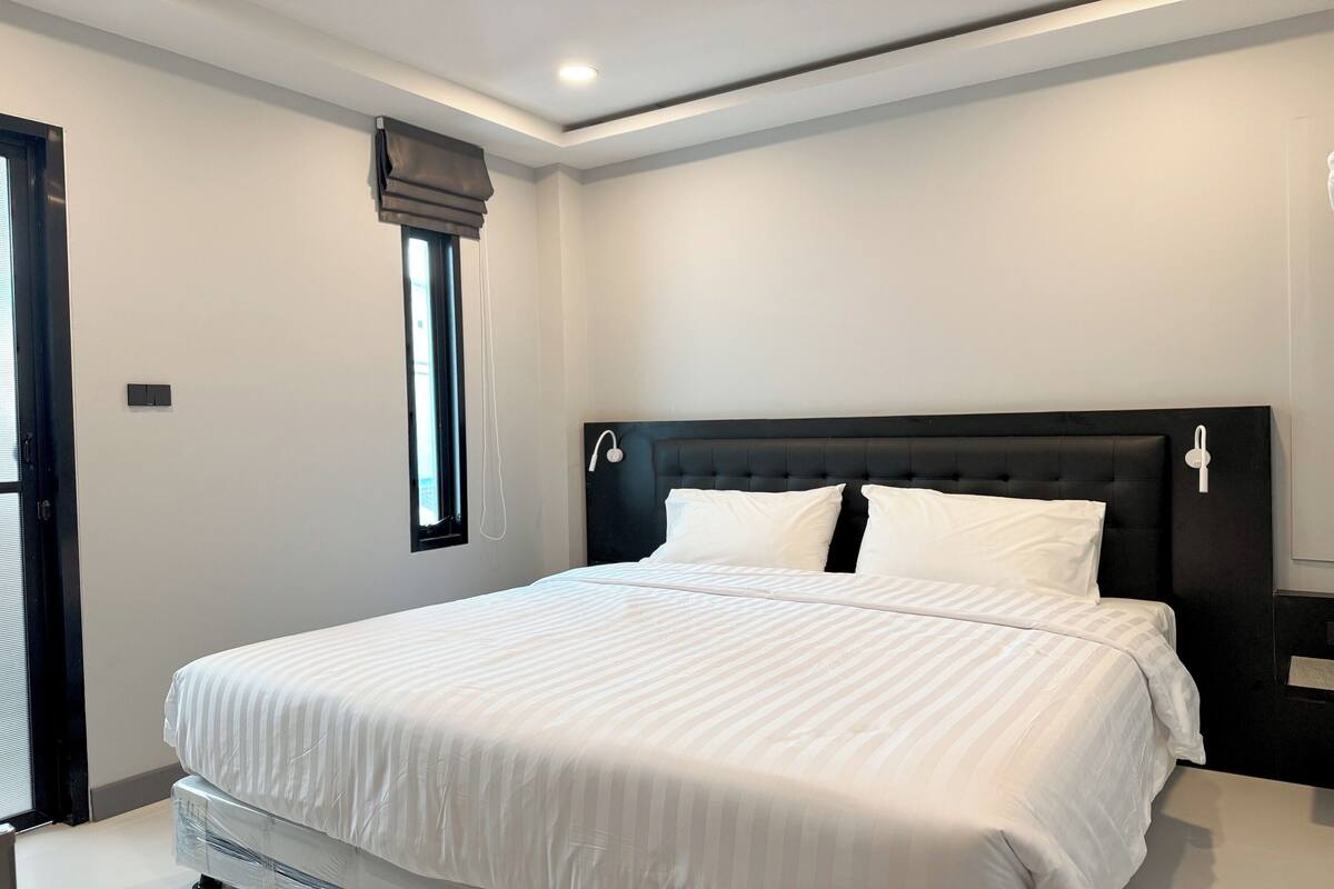 A modern bedroom with a large bed, a dark headboard, and a window with curtains.