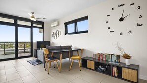 A modern living room with a dining area, large windows, and a wall clock. - Coburg Loft – 270° Views Skyline Escape (Coburg)