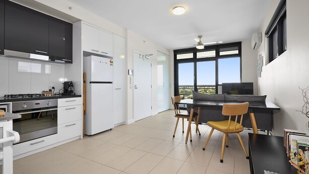 A modern kitchen with white cabinets, a black countertop, and a dining area with a table and chairs. - Coburg Loft – 270° Views Skyline Escape (Coburg)