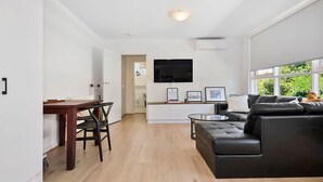 A modern living room with a black leather sofa, a dining table with chairs, a small coffee table, and a TV mounted on the wall. - The Nest Elwood - Beachside Escape with Free Parking (Elwood)
