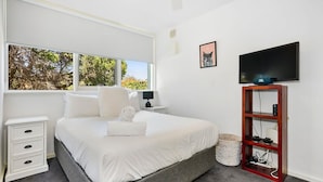 A modern bedroom with a large bed, a bedside table, a TV, and a view of trees through the window. - The Nest Elwood - Beachside Escape with Free Parking (Elwood)