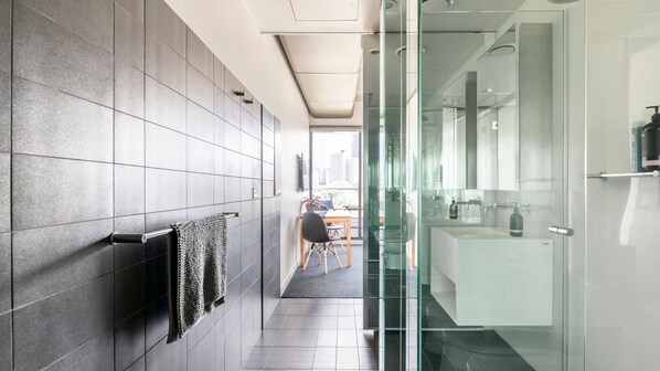 Un baño moderno con cabina de ducha de vidrio, lavamanos a la vista y un perchero para toallas.
