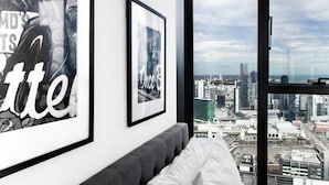 A modern room with a large window overlooking a cityscape, framed artwork on the wall, and a grey sofa with white cushions.