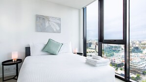 A modern hotel room with a large bed, a view of the city, and a minimalist design.