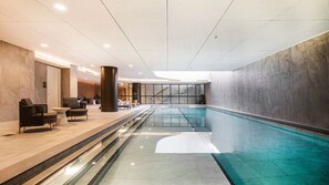 A modern indoor swimming pool with a glass barrier, lounge area with seating, and a view of the sky through the ceiling. - The Atrium - Resort-Style Glen Waverley Stay with Parking (Glen Waverley)