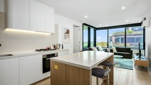 A modern kitchen with a central island, a dining area with a sofa and chairs, and large windows offering a view of the city. - The Atrium - Resort-Style Glen Waverley Stay with Parking (Glen Waverley)