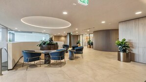 A modern reception area with a curved desk, blue chairs, and potted plants. - The Atrium - Resort-Style Glen Waverley Stay with Parking (Glen Waverley)