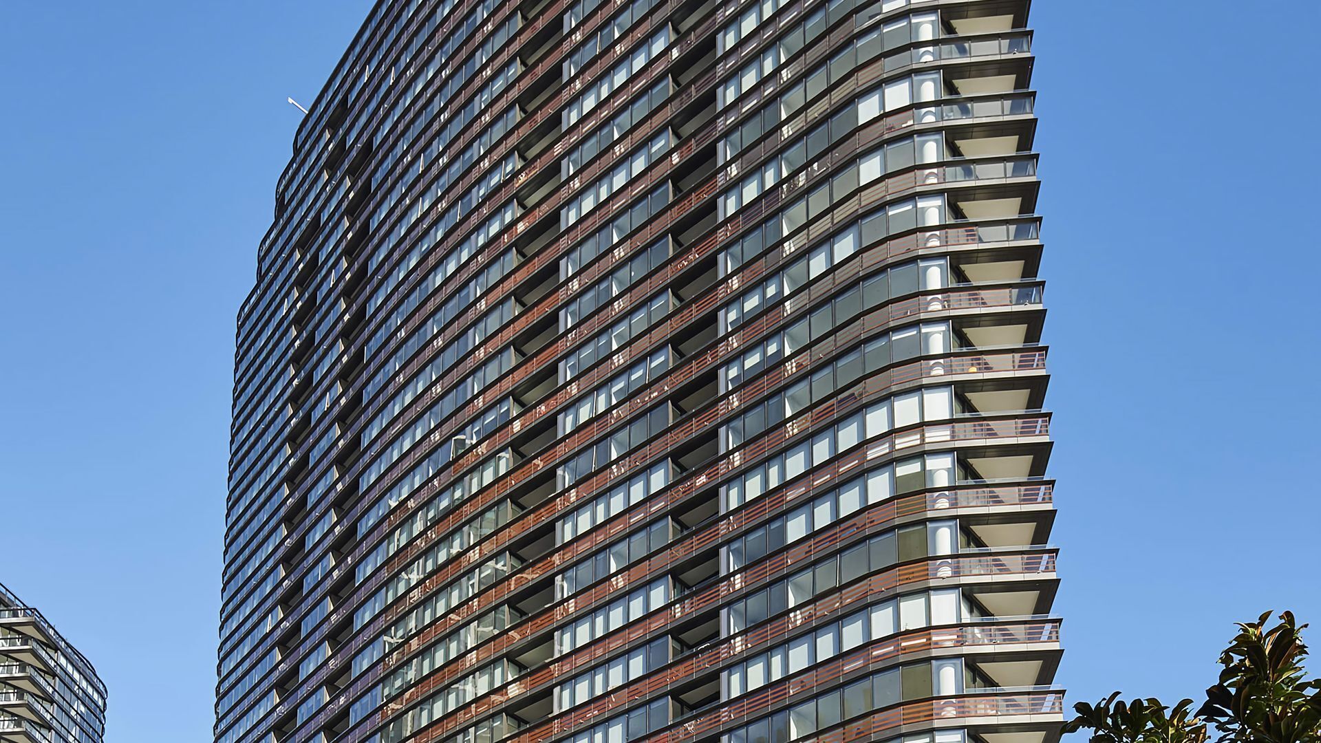 Ein hoch aufragendes Gebäude mit modernem architektonischen Design, das zahlreiche Balkone und einen klaren Himmel zeigt.