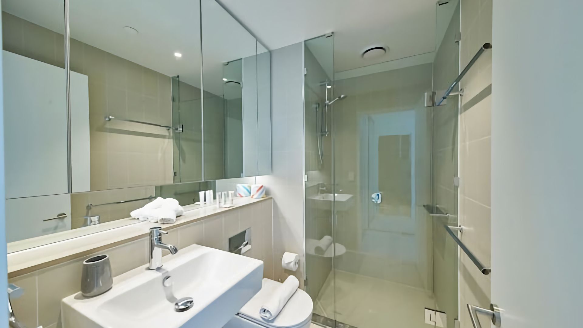 A modern bathroom with a glass-enclosed shower, a sink with a mirror, and a toilet.