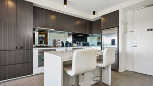 Una cocina moderna con armarios de madera oscura, una isla central con taburetes de bar y un refrigerador de acero inoxidable.