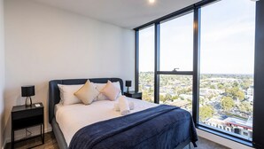A modern bedroom with a large window, a bed, two bedside tables, and a view of a cityscape.